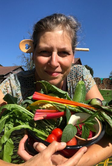 Nicole Frey mit Kochlöffel im Haar und Sieb gefüllt mit Gemüse in der Hand mit blauem Himmel im Hintergrund